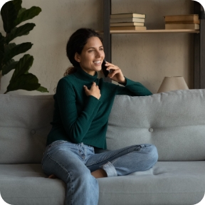 Woman lounges on a couch and smiles while speaking on the phone.